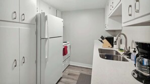 A kitchen with white cabinets, a refrigerator, a stove, a sink, and a coffee maker. - Lansing Layover #4 | New York State of Mind (Lansing)