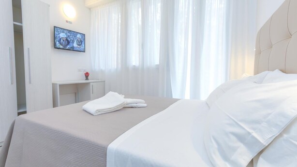A hotel room with a bed, a TV on the wall, a desk, and a wardrobe. - Hotel Tourist Meuble (Rimini)