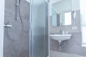 A modern bathroom with a glass-enclosed shower, a white sink, and a hairdryer mounted on the wall. - Hotel Tourist Meuble (Rimini)