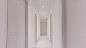 A long, narrow hallway with white walls and a tiled floor, leading to a door at the end. - Hotel Tourist Meuble (Rimini)