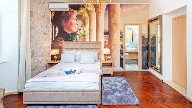 Een slaapkamer met een groot bed, een kroonluchter, een stenen muur en een badkamer door een open deur zichtbaar.