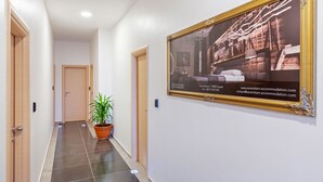 Een hotelgang met een ingelijst schilderij aan de muur, een potplant en een betegelde vloer.