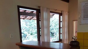 Una cucina con angolo bar, due sgabelli in legno, una finestra con tende e uno schienale piastrellato.