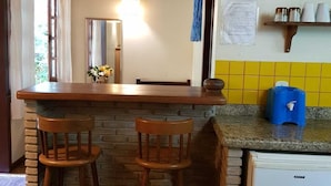Una cucina con angolo bar, sgabelli di legno, un frigorifero e una dispensa piena di utensili da cucina.