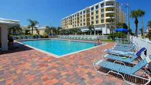 Ein Hotelpoolbereich mit großem Pool, Liegestühlen und einem mehrstöckigen Gebäude im Hintergrund.