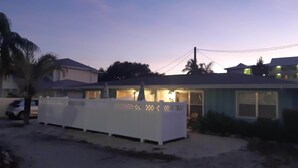 Ein Wohnhaus mit eingezäunter Vorderseite, einem parkenden Auto und einer Palme.