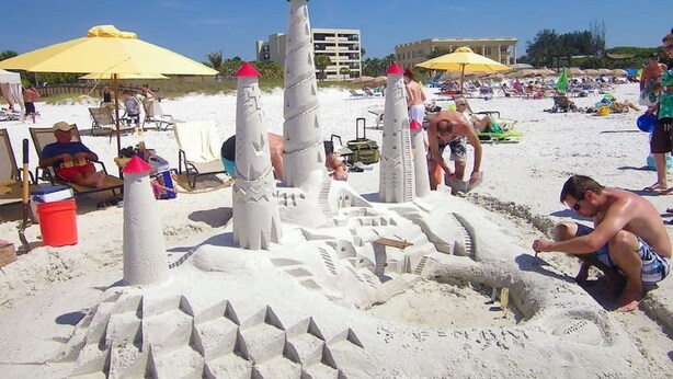 Eine Strandansicht mit einer großen Sandburg und Menschen in der Nähe.