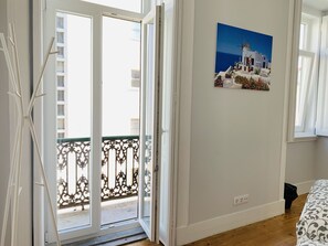A room with a balcony, a painting of a coastal scene, and a bed with a patterned bedspread. - Memory of Lisbon (Lisbon)