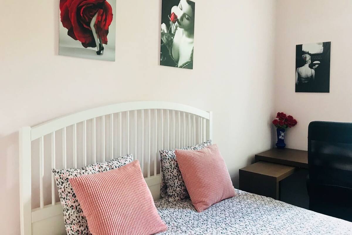 A bedroom with a white headboard, two patterned pillows, a bedspread, and three artworks on the wall.