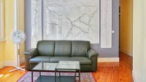 A living room with a grey leather sofa, a glass coffee table, a standing fan, and a large marble-patterned wall. - Memory of Lisbon (Lisbon)
