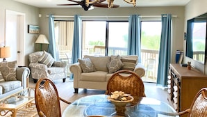A spacious living room with a large sofa, a dining table with chairs, a chandelier, and a balcony with blue curtains. - Relaxing getaway, with picturesque views, & a short walk to St. Augustine beach. (St. Augustine)