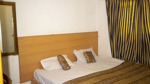 Une chambre d’hôtel avec une tête de lit en bois, du linge de lit blanc et des rideaux à rayures.