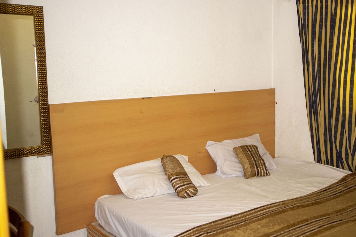 A hotel room with a wooden headboard, white bedding, and striped curtains.