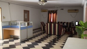 Une pièce avec un sol à carreaux, un bureau avec un paravent, un ensemble de meubles de salon et un téléviseur.