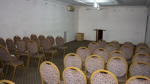 Une salle de conférence avec des rangées de chaises, un pupitre et un appareil de climatisation fixé au mur.