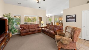 A spacious living room with a brown leather sectional sofa, a patterned armchair, and a flat-screen TV. - Exceptional 4 Bedroom Vacation Home near Palmer Golf Course (Mesquite)