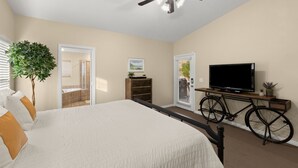 A bedroom with a bed, a ceiling fan, a television on a stand, a bicycle, and a door leading to a bathroom. - Exceptional 4 Bedroom Vacation Home near Palmer Golf Course (Mesquite)