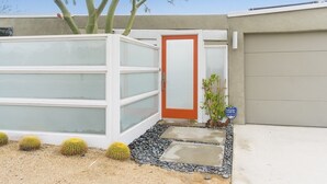 Una casa moderna con un garaje con paredes de vidrio, una puerta roja y un letrero con motivos desérticos.