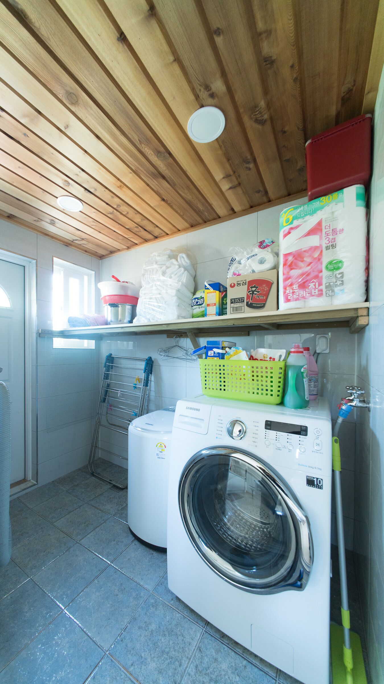 A laundry area with a washing machine, shelves with various items, and a drying rack.