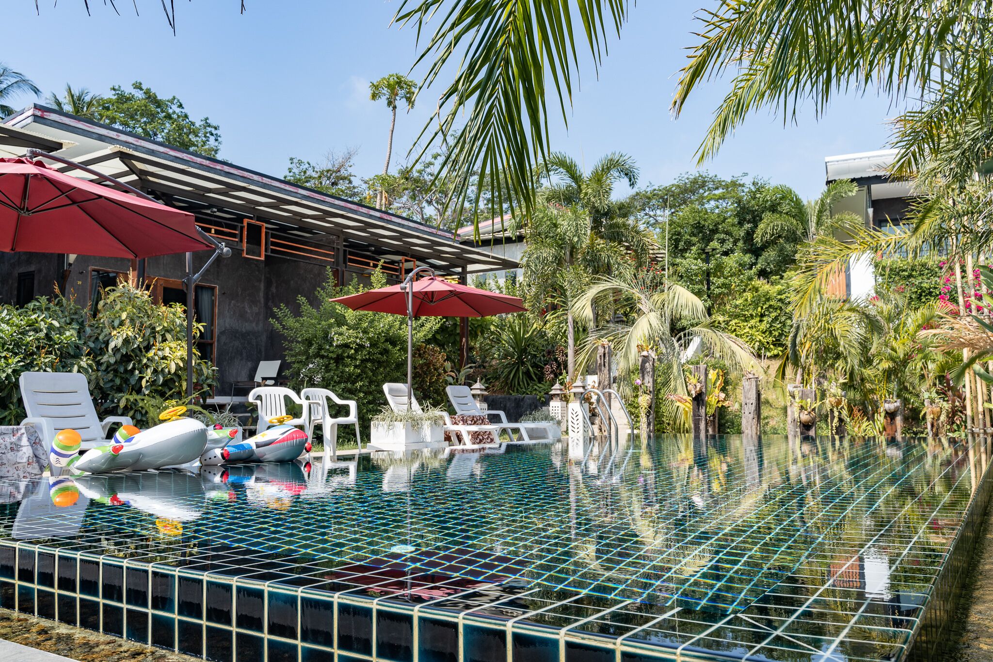 Un área de piscina con sillones de descanso, sombrillas y una piscina con azulejos.