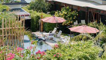 A pool area with lounge chairs and umbrellas, surrounded by lush greenery and flowers.