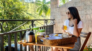 A balcony with a table set for breakfast, including a kettle, a fruit bowl, and a basket with bread and eggs. - Chalés Santa Catarina (Socorro)
