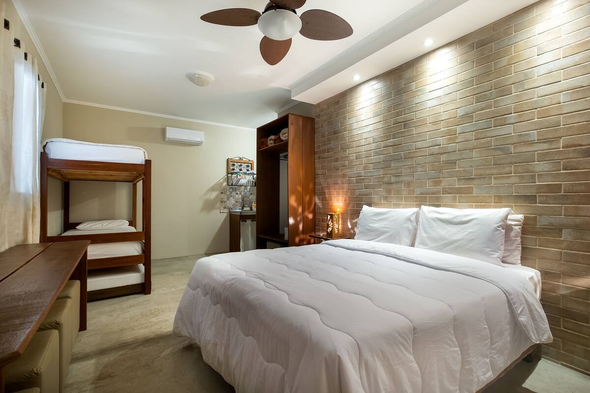 A hotel room with a bunk bed, a desk, a wardrobe, and a brick-patterned wall.