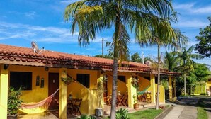 A yellow building with a red-tiled roof, a hammock, and palm trees. - Chalés Santa Catarina (Socorro)
