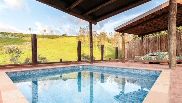 A swimming pool with a clear view of a green landscape and a wooden deck area. - Chalés Santa Catarina (Socorro)