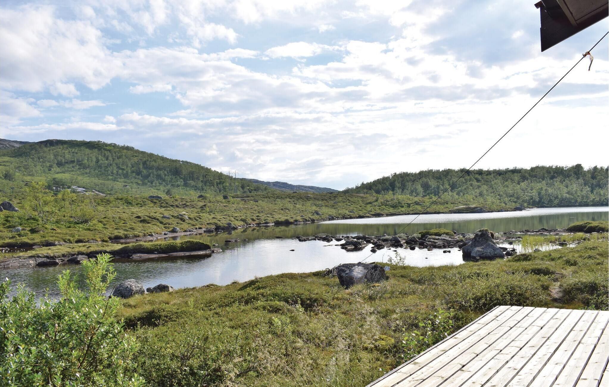 A wooden deck overlooking a lake with surrounding greenery and hills.
