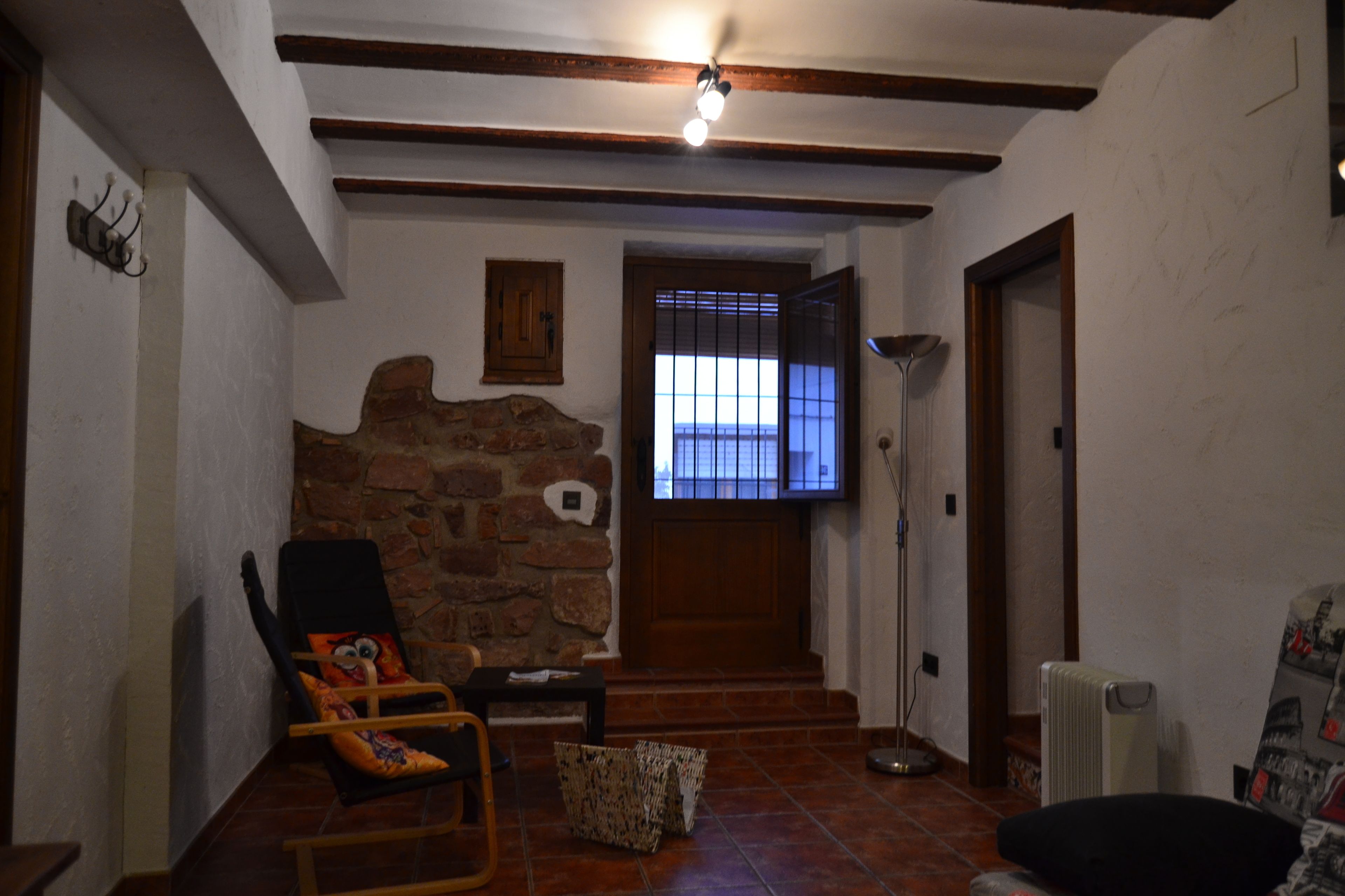 A cozy living room with a stone wall, a wooden ceiling, and a large window with bars.