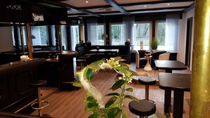 Un intérieur de restaurant moderne avec un plancher en bois, un bar, des espaces de repos et de grandes fenêtres qui laissent entrer la lumière naturelle.