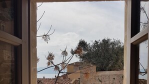 Blick durch ein offenes Fenster auf einen Innenhof mit Steinmauern, einem Ziegeldach und felsigem Untergrund.