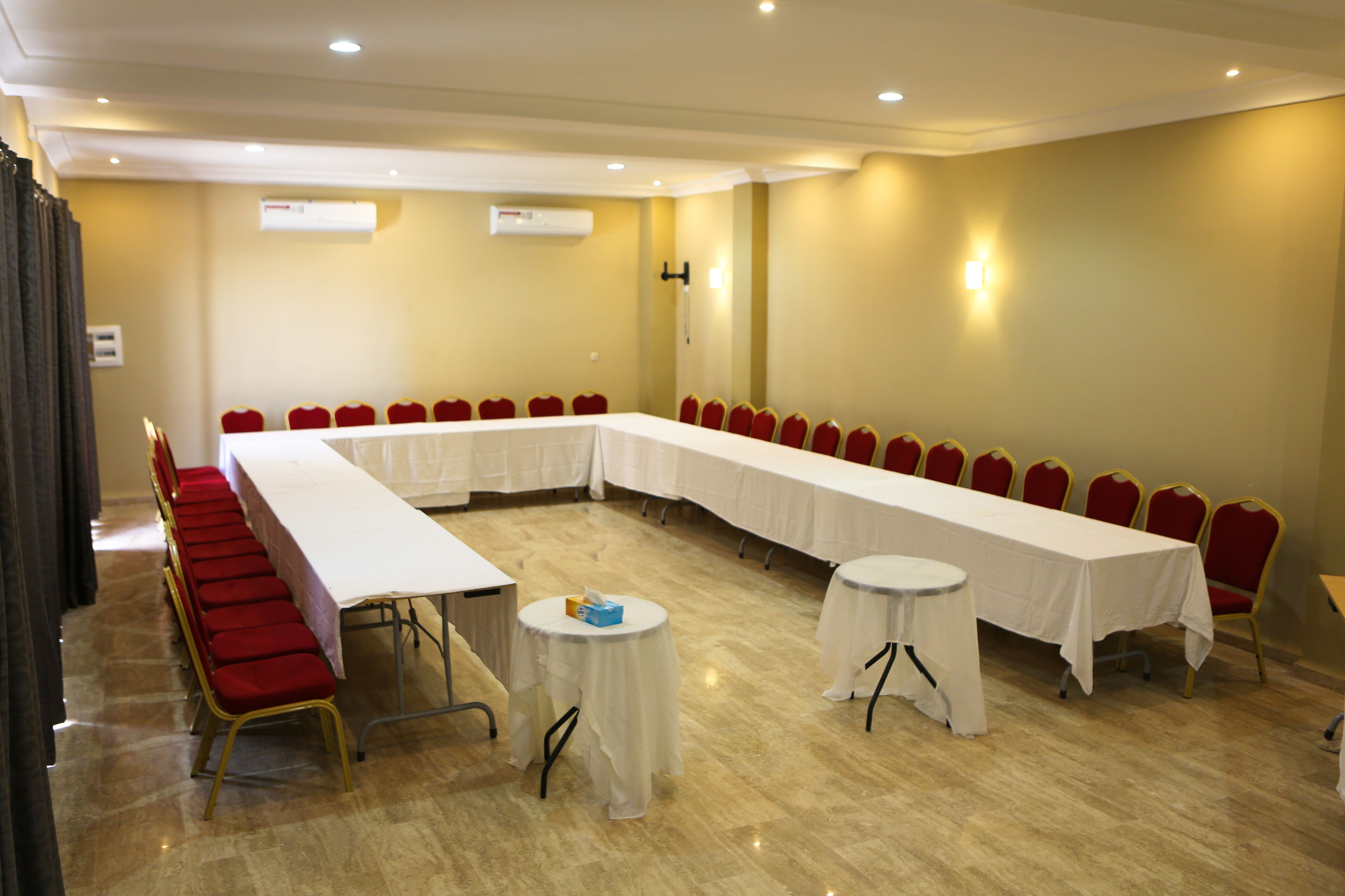 Un salón de conferencias con una larga mesa, sillas rojas y dos pequeñas mesas redondas.