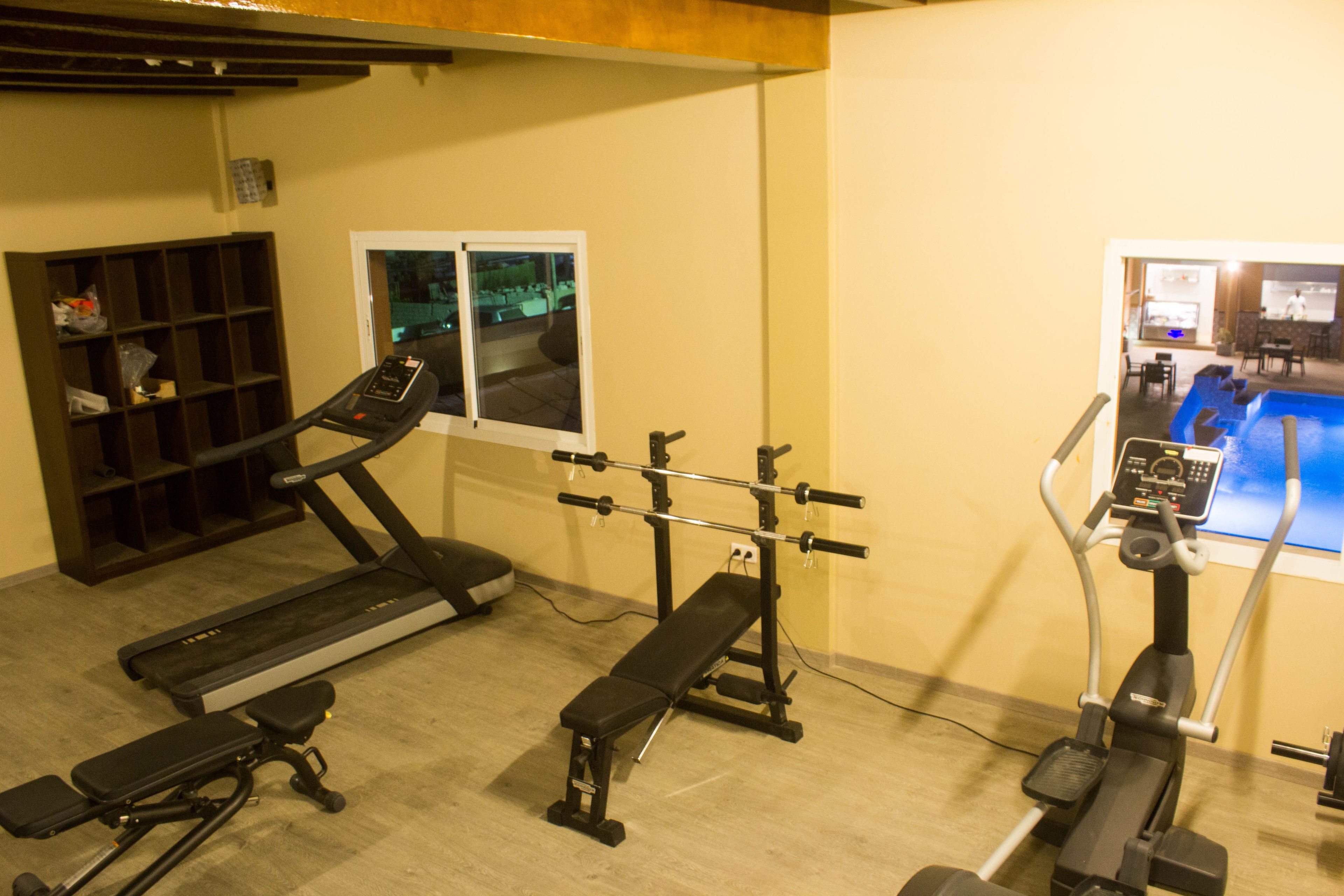 Une salle de sport équipée d’un tapis de course, d’un banc de musculation et d’un appareil elliptique.