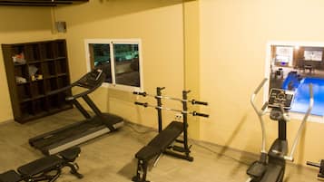 Une salle de sport équipée d’un tapis de course, d’un banc de musculation et d’un appareil elliptique.
