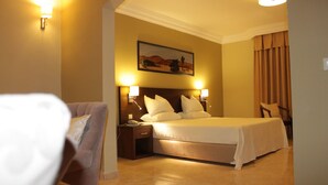 Una habitación de hotel con una cama grande, dos lámparas de noche, una mesita de noche, una silla y un cuadro en la pared.