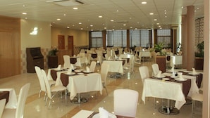 Un comedor amplio con varias mesas y sillas dispuestas en filas, con ventanas grandes que aportan luz natural.