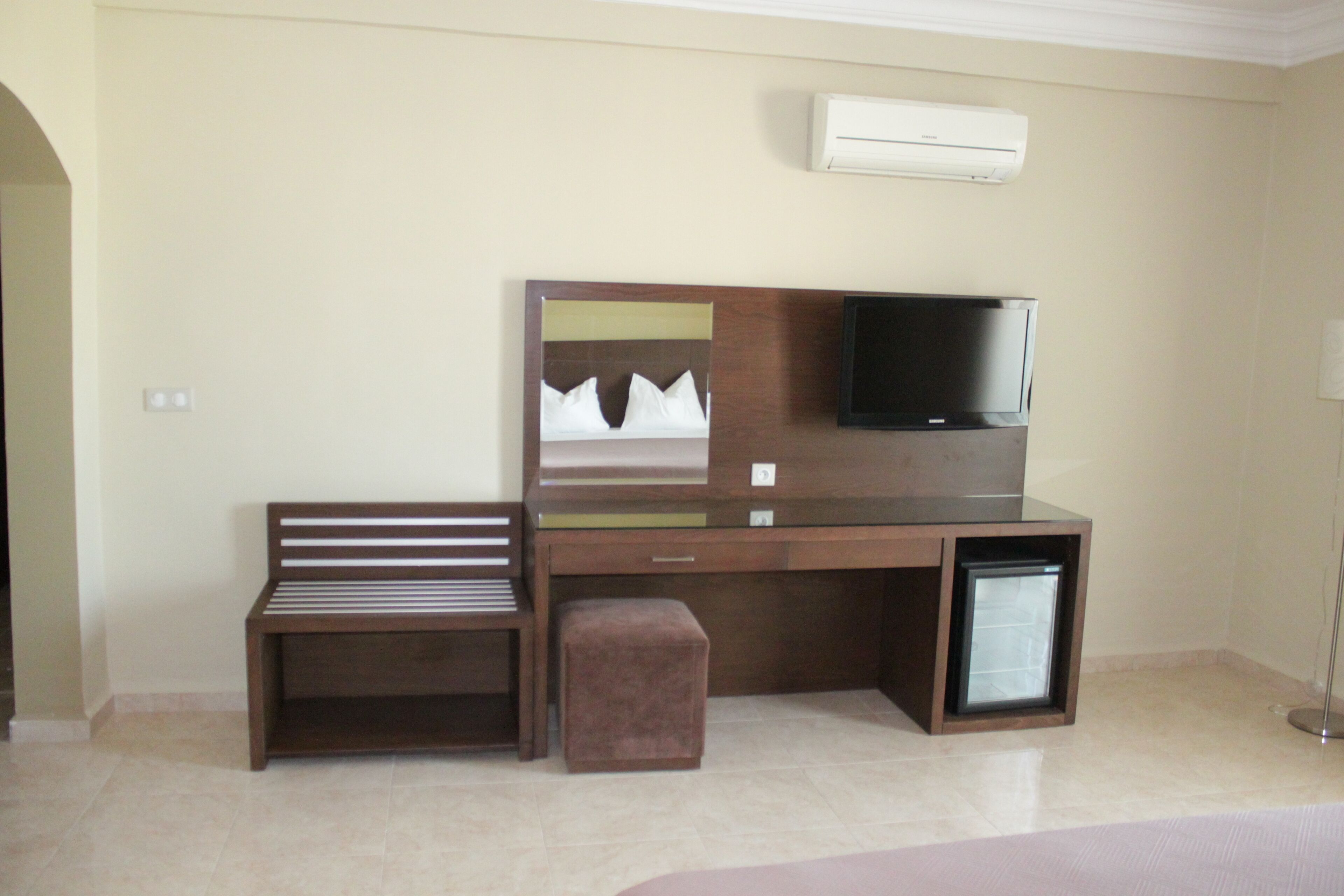 Ein Hotelzimmer mit einem Holztisch, einem Fernseher, einer Bank und einer Klimaanlage.