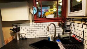 A kitchen with a black countertop, white cabinets, a stainless steel sink, and a window with red trim. - Two Rivers Relaxing Retreat  (Portland)
