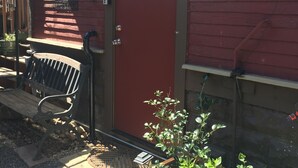A red wooden building with a door, a bench, and a planter with green plants. - Two Rivers Relaxing Retreat  (Portland)