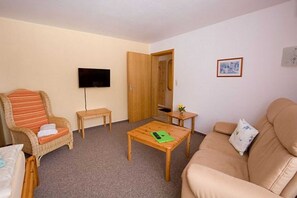 A living room with a sofa, a chair, a coffee table, a television, and a door.