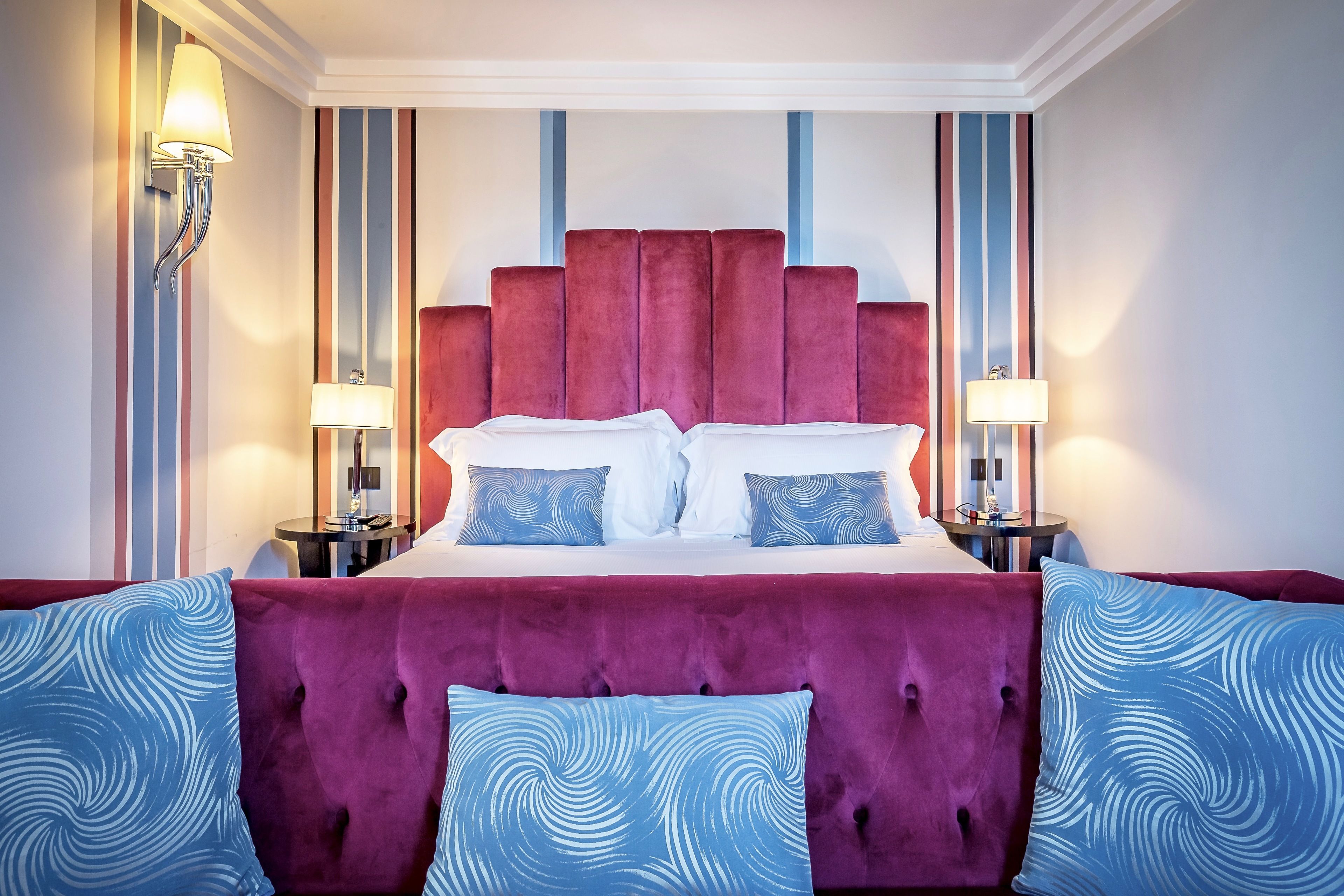 A hotel room with a large bed, two bedside tables, and a red headboard.