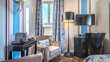 A hotel room with a bed, a desk with a computer, a chair, a lamp, and curtains.