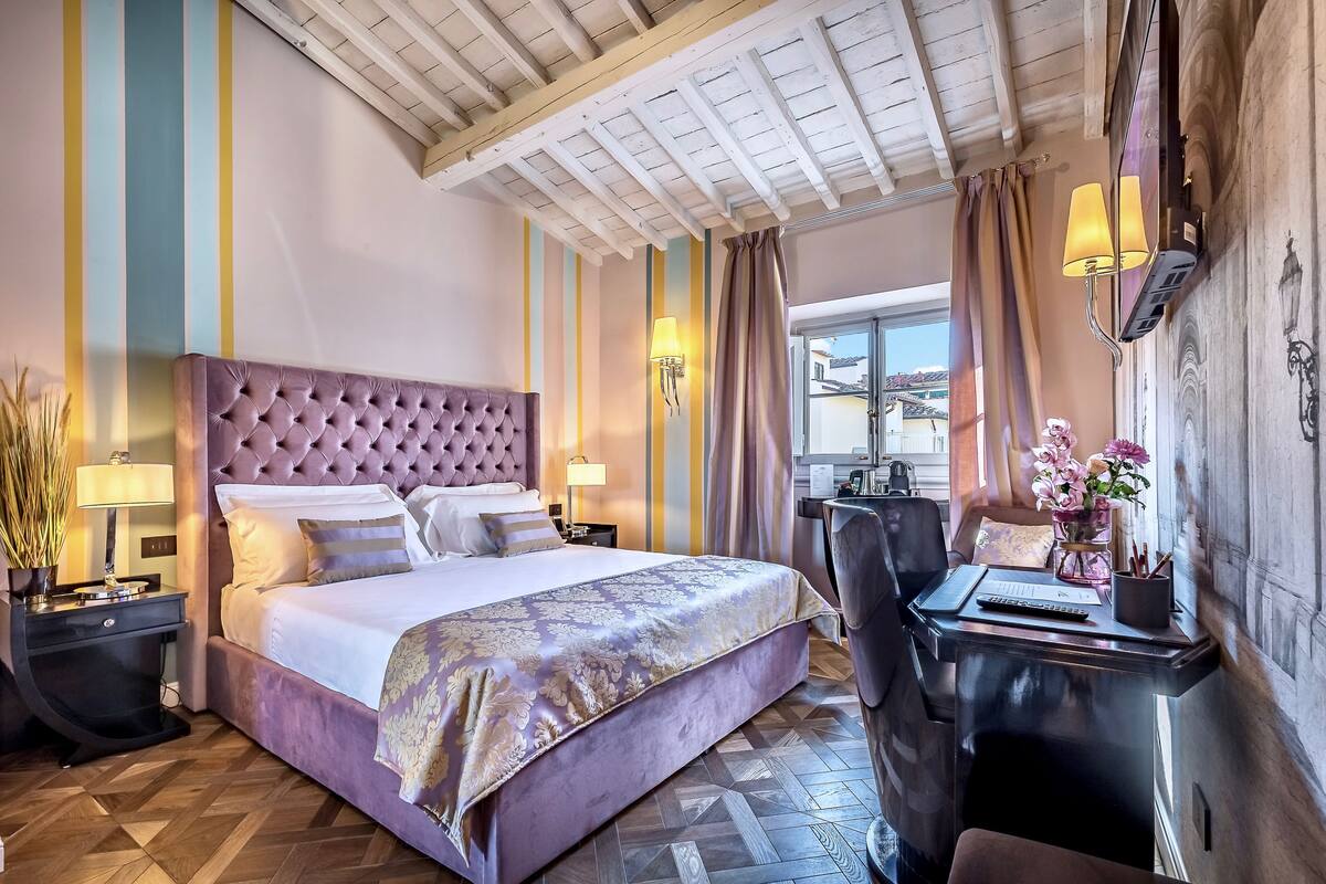 A hotel room with a large bed, a desk with a lamp, and a view of the outside.