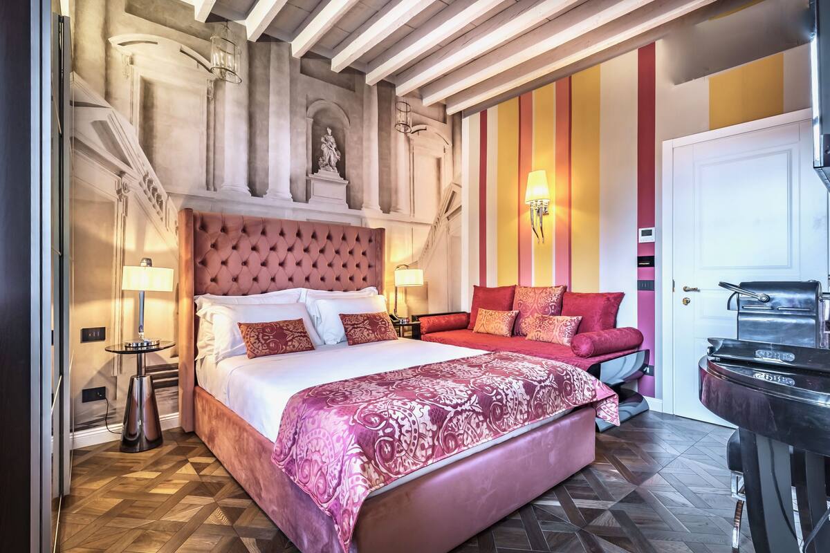 A bedroom with a large bed, a second bed, a piano, and a wall with vertical stripes.