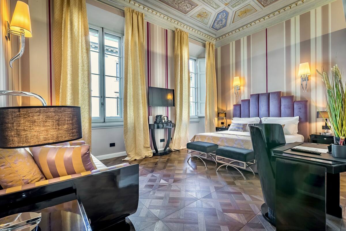 A hotel room with a bed, a desk, a chair, a TV, and a window with curtains.