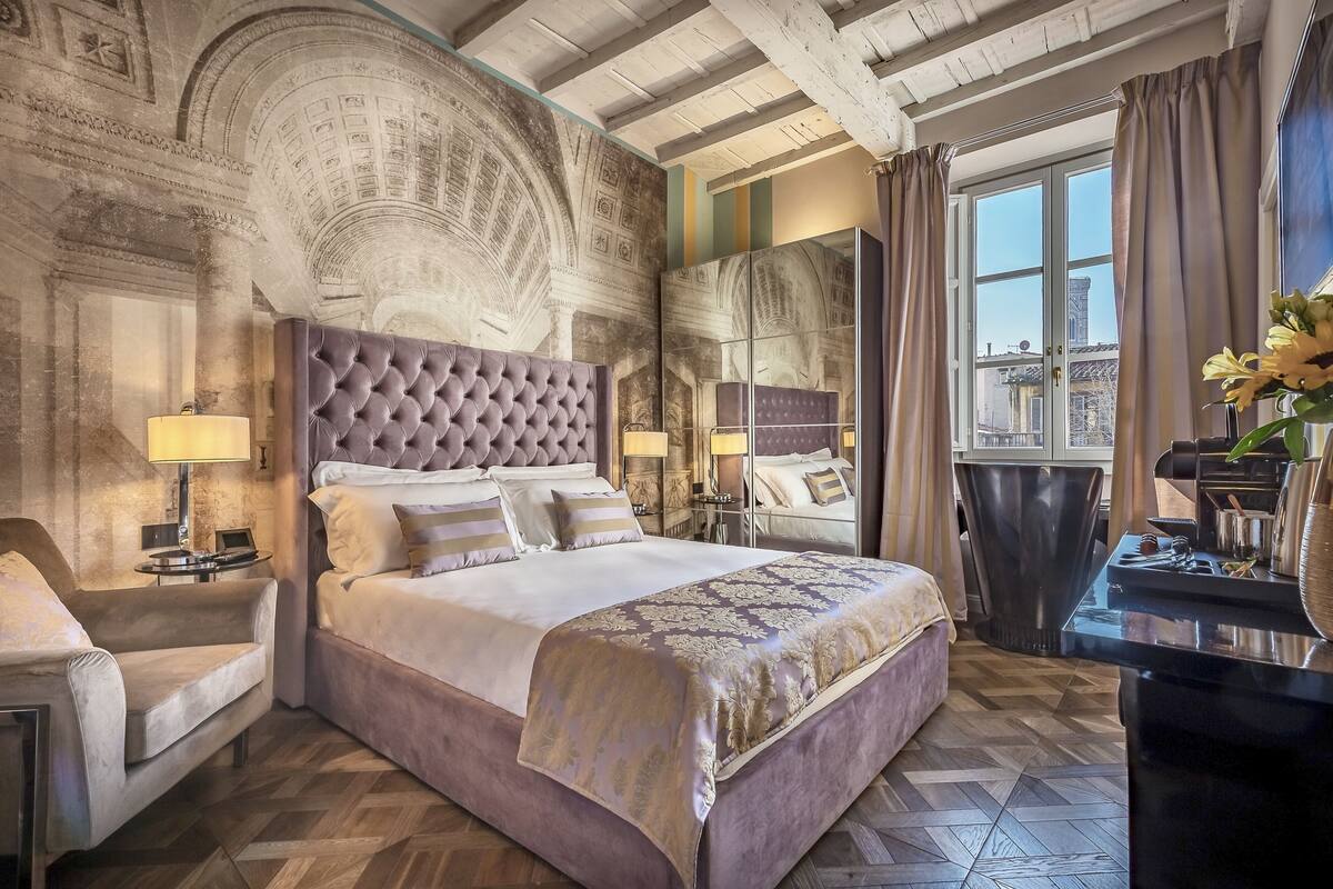 A luxurious bedroom with a large bed, a tufted headboard, and a view of the city through a large window.