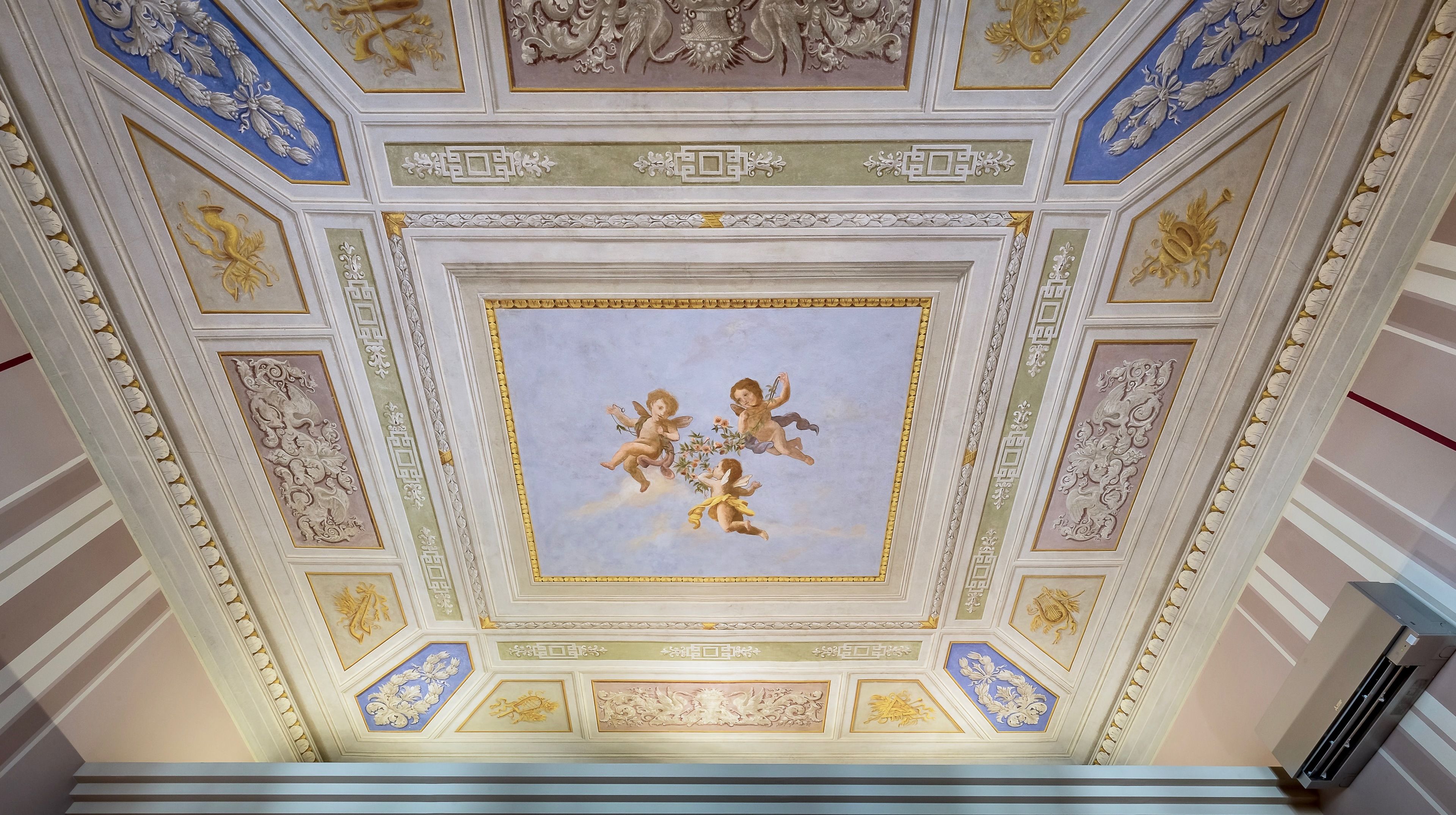 A ceiling with intricate carvings and a central fresco of cherubs.