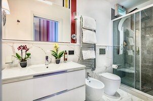 A modern bathroom with a white sink, two potted plants, a toilet, and a glass-enclosed shower.